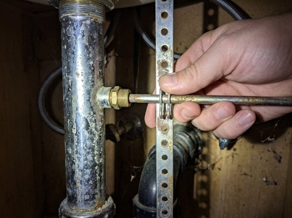 Hand adjusting a sink pop-up pivot rod in the clevis strap under a bathroom vanity