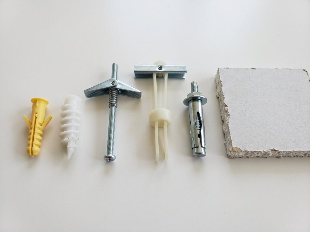 Five types of drywall anchors side by side: plastic expansion, self-drilling, spring toggle, strap toggle and molly bolt
