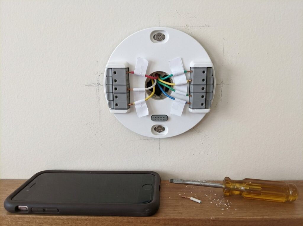 Thermostat base plate on a wall with tagged red, white, yellow, green and blue low-voltage wires in its terminals