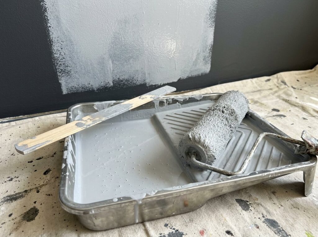 Roller tray with gray tinted primer in front of a dark wall partly covered with primer