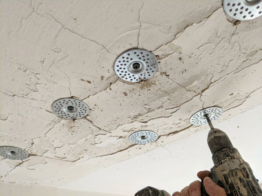 Perforated plaster washers screwed into a cracked plaster ceiling to reattach loose plaster