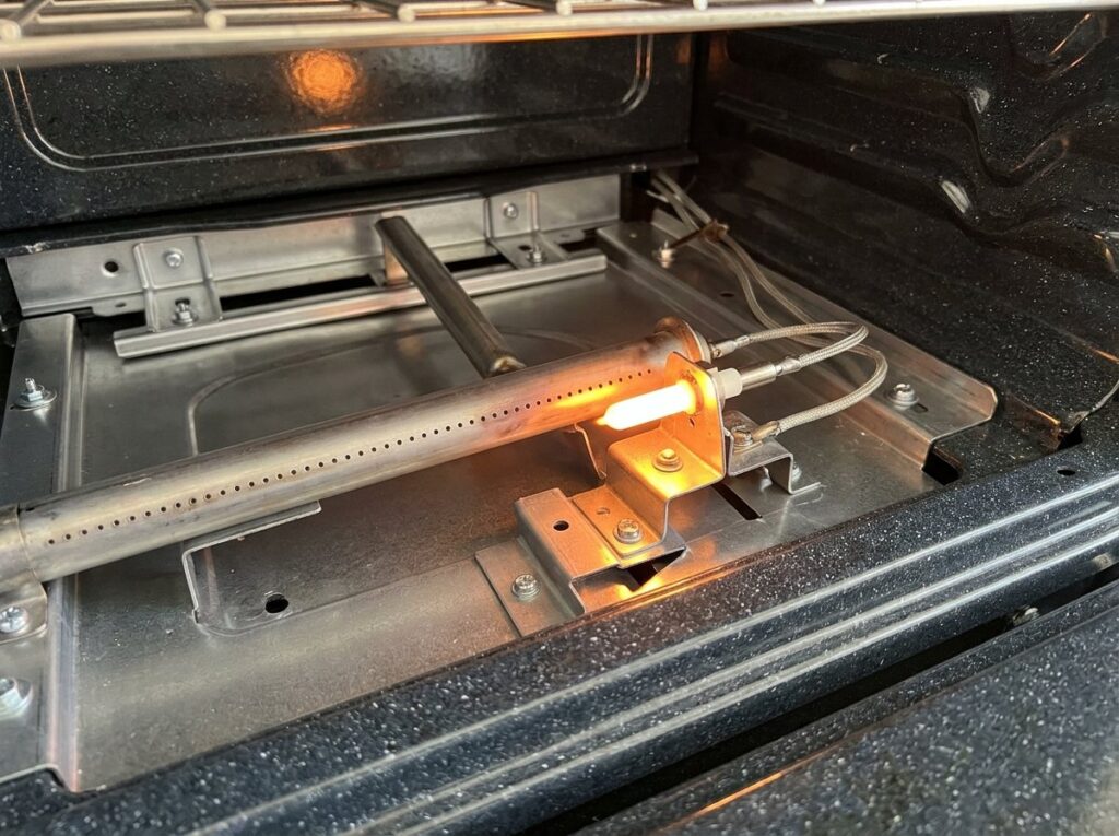 Gas oven igniter glowing bright orange beside the burner tube with no flame lit